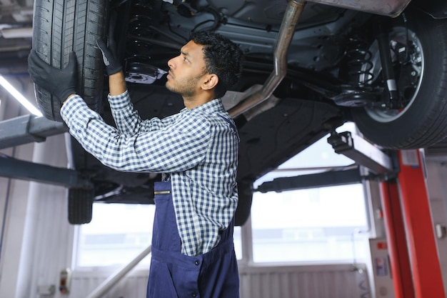 Il meccanico ispanico latino in uniforme sta esaminando un'auto mentre lavora nel servizio auto