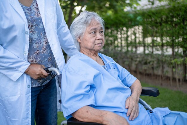 Il medico aiuta e si prende cura di una donna anziana o anziana asiatica paziente seduta su una sedia a rotelle al parco