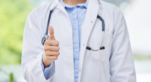 Il medico alza il pollice e la mano di un impiegato medico grazie gesto sanitario su sfondo sfocato Mani di un chirurgo esperto con stetoscopio nel segno sì o nell'accordo per il successo della salute