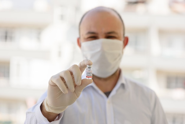 Il medico con i guanti bianchi tiene la bottiglia con il vaccino COVID-19