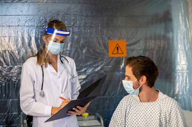 Il medico con maschera protettiva e cartella sta visitando il paziente.