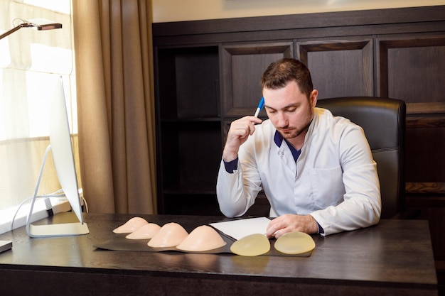 Il medico consiglia il paziente seduto al tavolo al centro della chirurgia plastica. Salute e medicina. Sul tavolo ci sono le protesi mammarie.