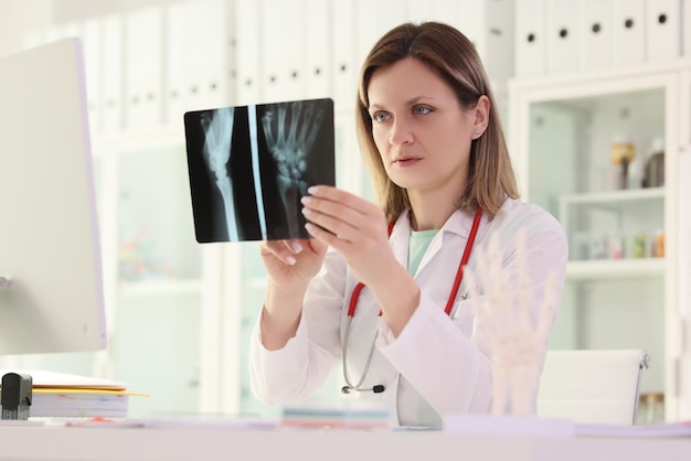 Il medico della donna studia l'immagine dei raggi X del braccio del paziente seduto al tavolo nella premessa della clinica