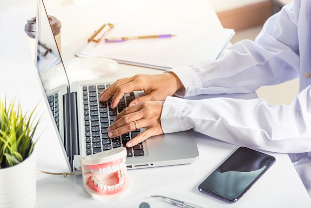 Il medico dentista o l'infermiere in uniforme usa i raggi X dei denti del software orale e digita il modulo di anamnesi medica nel computer portatile