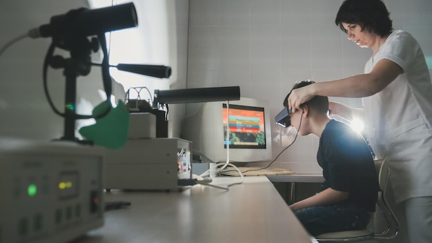 Il medico di oftalmologia controlla la visione del ragazzo con l'aiuto di occhiali per realtà virtuale stereovideo, grandangolo