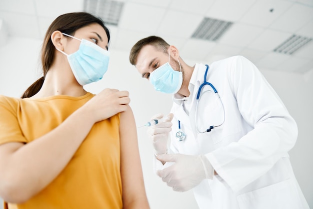 Il medico fa un'iniezione nella spalla di un paziente con una maschera medica vista dal basso vaccinazione covid