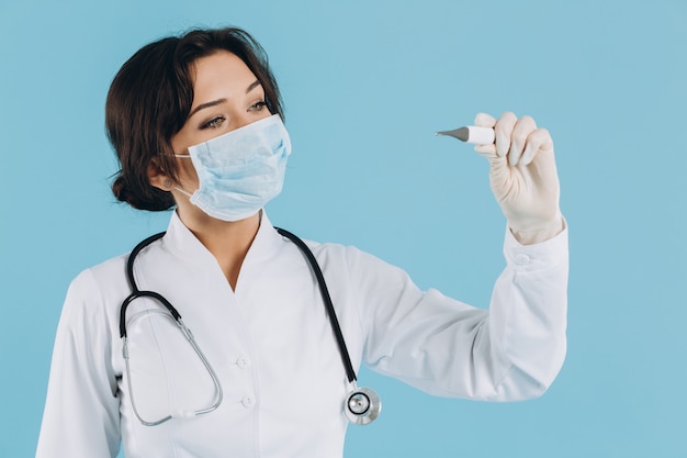 Il medico femminile nella maschera con lo stetoscopio tiene il termometro elettrico. Concetto COVID-19