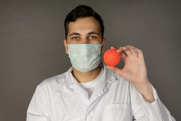 il medico indossa una maschera e tiene in mano un modello di coronavirus.