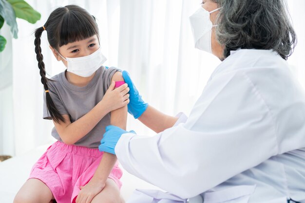 Il medico sta applicando il cerotto medicinale dopo la vaccinazione sulla spalla di bambine asiatiche in ospedale