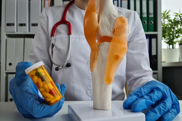 Il medico sta tenendo le pillole e il modello del ginocchio e della gamba