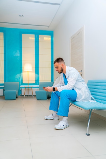 Il medico stanco in scrub riposa sul divano nella sala clinica Giovane medico dopo una pesante giornata di lavoro Concetto di assistenza sanitaria