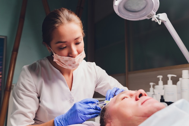 il medico traccia un punto per iniezioni sul viso del paziente. preparazione per la biorivitalizzazione da vicino.