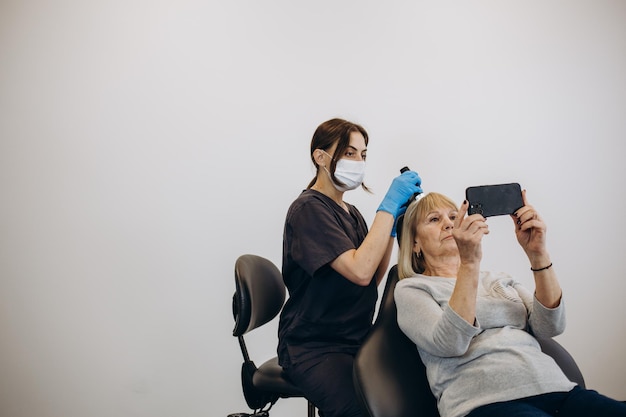 Il medico tricologo esamina i capelli della paziente utilizzando il tricoscopio in clinica Procedura di tricoscopia dei capelli Esegue un tricoscopio sul cuoio capelluto e osserva i risultati sullo schermo del monitor Tricoscopia del computer