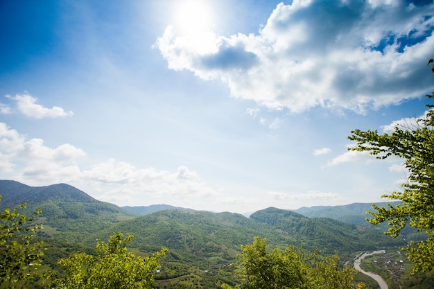 Il meraviglioso scenario della montagna verde è sullo sfondo del cielo nuvoloso blu con un sole.