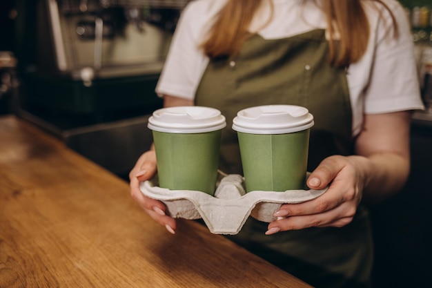 Il miglior caffè da asporto Parte della giovane donna allegra in grembiule che tiene tazze da caffè mentre si trova al bar