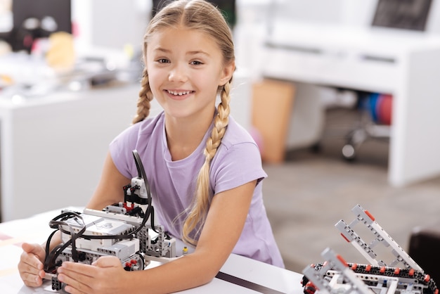 Il mio nuovo amico informatico. Sorridente ragazza felice felice seduta nel laboratorio di robotica e tenendo cyber robot mentre esprime gioia