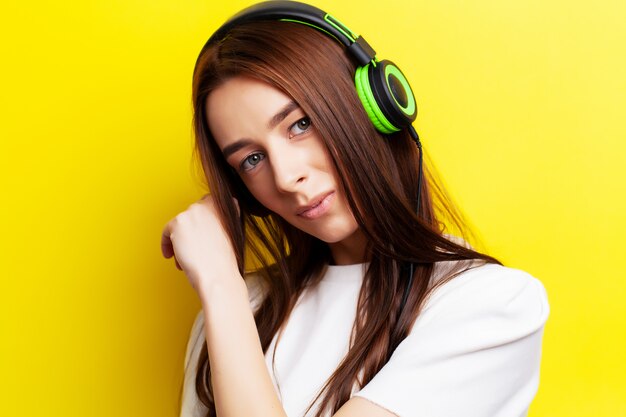 Il modello della bella ragazza ascolta musica in cuffie su giallo