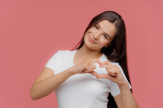 Il modello femminile castana piacevole sorridente modella il segno del cuore