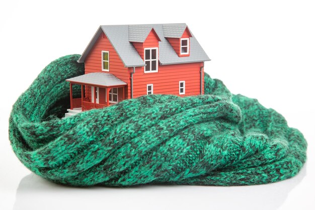 Il modello House è isolato con una sciarpa lavorata a maglia su uno sfondo bianco il concetto di mantenere caldo e accogliente al chiuso a casa protezione dal freddo