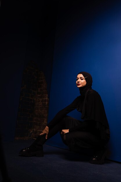Il modello musulmano di moda in hijab nero sta posando su sfondo blu nella foto creativa della religione dell'Islam in studio