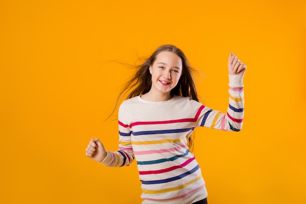 Il modello teenager della ragazza posa su un fondo giallo in una giacca a strisce multicolore. Emozioni, spazio per il testo