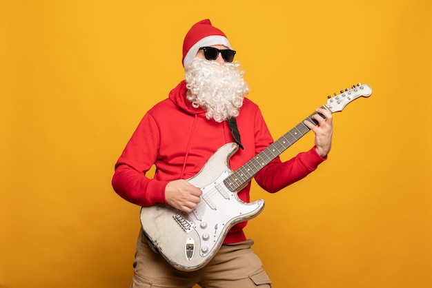 Il moderno Babbo Natale rock n roller suona la chitarra emotivamente isolato su sfondo giallo