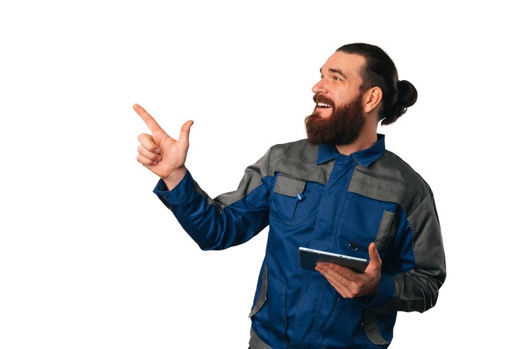 Il moderno tuttofare barbuto che indossa l'uniforme tiene in mano un tablet mentre indica da parte