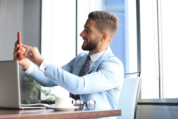 Il moderno uomo d'affari sorridente sta facendo un selfie in ufficio.