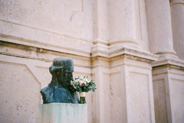 Il monumento dell'uomo con il cappello sta annusando il bouquet da sposa di rami di rose di peonie rosa e bianche