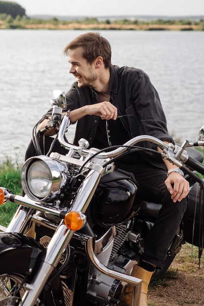 Il motociclista alla moda e bello è seduto e si sta rilassando sulla sua moto all'aperto