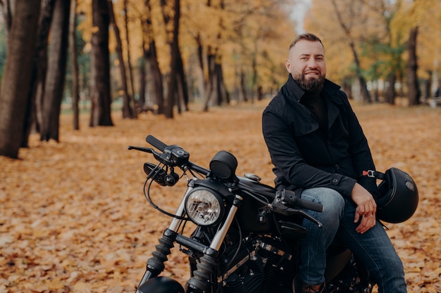 Il motociclista maschio barbuto guida la bici nera, tiene il casco, ha viaggiato da solo