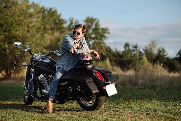 Il motociclista maschio bello che indossa i vestiti dei jeans è seduto sulla moto