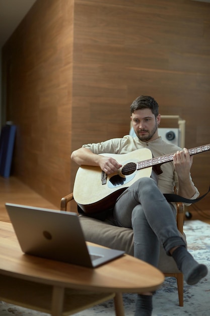 Il musicista creativo suona la chitarra acustica guardando la lezione musicale online sul laptop mentre si esercita a casa e l'apprendimento