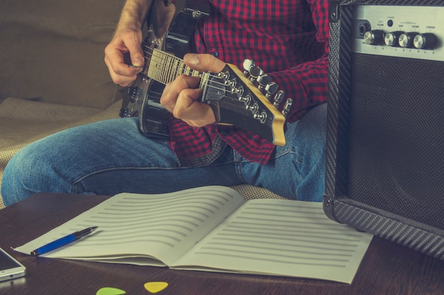 Il musicista si siede sul divano e suona la chitarra elettrica. prima di lui le note e una guita