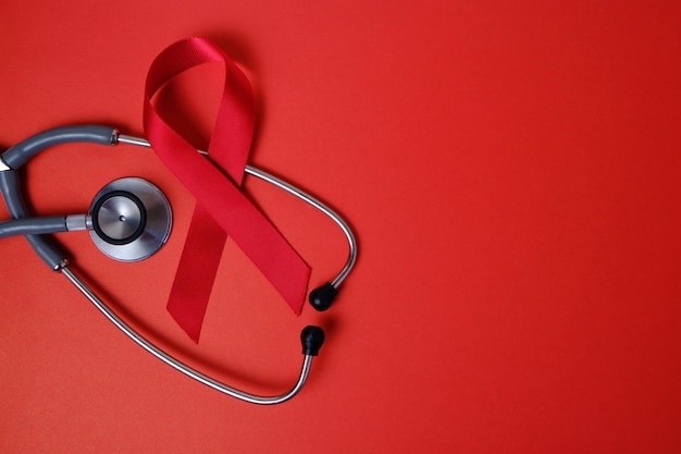 Il nastro rosso è un simbolo di AIDS, problemi di tossicodipendenza, stetoscopio su sfondo rosso.