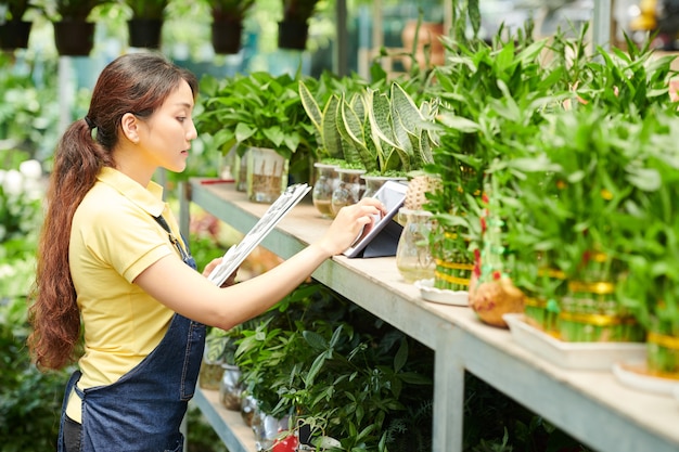 Il negozio di giovani piante femminili lavora con documenti e computer tablet controllando i fiori sugli scaffali e accettando ordini online dal cliente