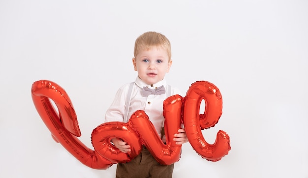 Il neonato del bambino in vestito tiene l'amore dell'iscrizione dai palloncini su un bianco.