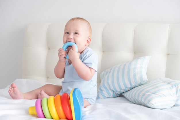 Il neonato divertente si siede sul letto e gioca con la piramide dei bambini del giocattolo.