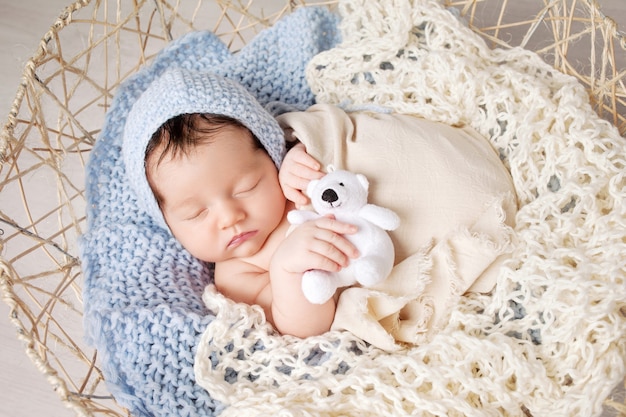 Il neonato dolce dorme in un cestino. Bello ragazzo appena nato con il giocattolo dell'orso.