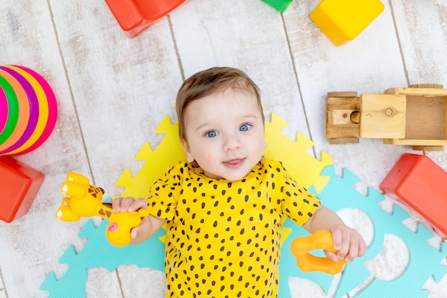 Il neonato felice sorridente gioca nella scuola materna in una tuta gialla con giocattoli colorati luminosi