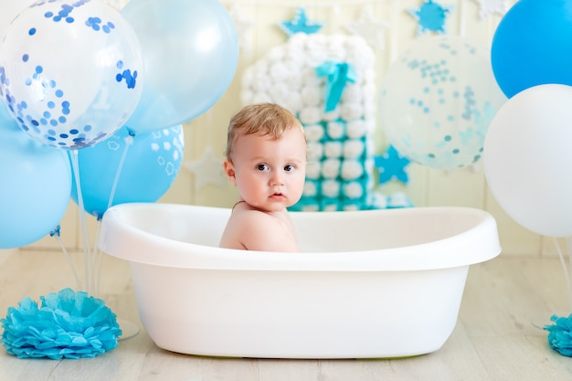 Il neonato festeggia il compleanno di 1 anno in una vasca da bagno con palloncini, bagnando il bambino con palloncini blu.