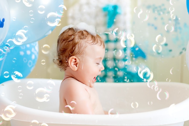 Il neonato festeggia il compleanno di 1 anno in una vasca da bagno con palloncini, bagnando il bambino con palloncini blu.