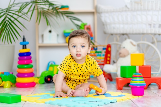 Il neonato gioca nella stanza dei bambini in un body giallo con giocattoli colorati luminosi