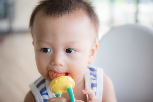 Il neonato sveglio asiatico sta mangiando la frutta dall&#39;accessorio.