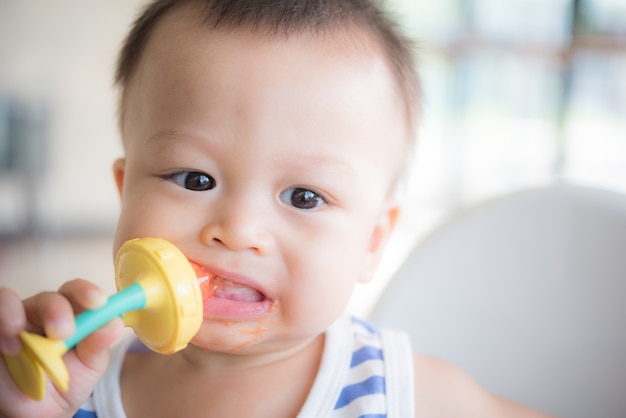 Il neonato sveglio asiatico sta mangiando la frutta dall&#39;accessorio.