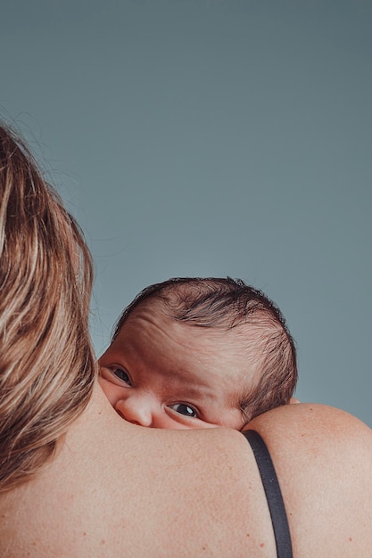 Il neonato tra le braccia di sua madre guarda la telecamera con un'espressione comprensiva