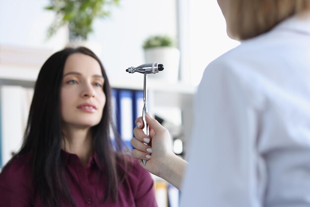 Il neurologo controlla i riflessi con un martello speciale mentre esamina la giovane paziente femminile in ufficio medico