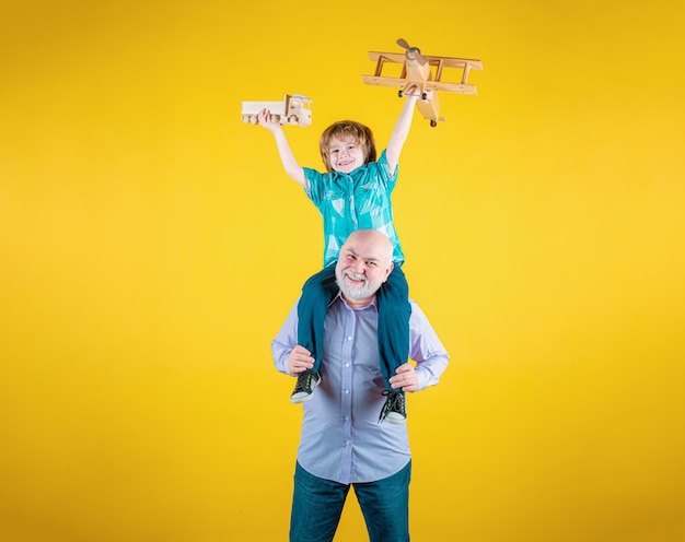 Il nonno e il nipote cavalcano sulle spalle con un aereo e un camion giocattolo di legno.