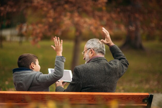 Il nonno e suo nipote trascorrono del tempo insieme nel parco. Sono seduti sulla panchina. Camminando