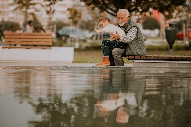 Il nonno trascorre del tempo con sua nipote presso una piccola piscina d'acqua nel parco il giorno d'autunno